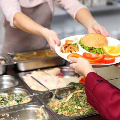 pleasant woman giving lunch to school girl in cafeteria